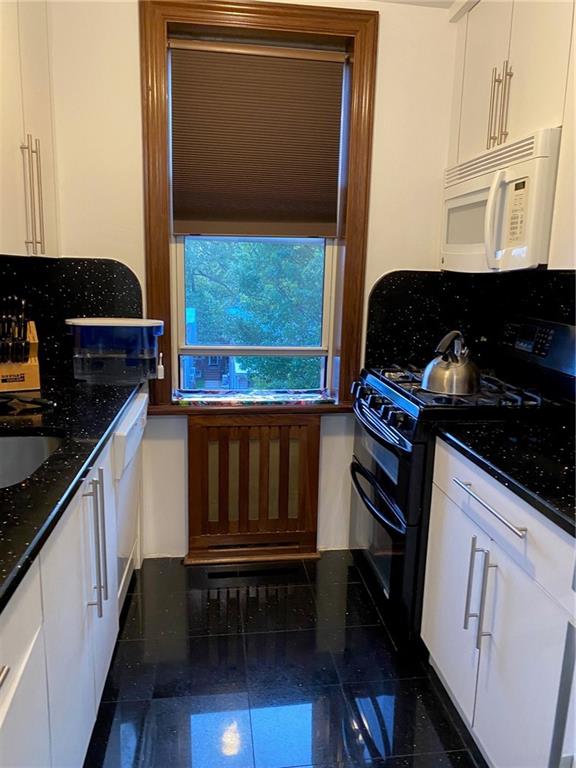 kitchen with double oven range, sink, white cabinets, and dark stone counters