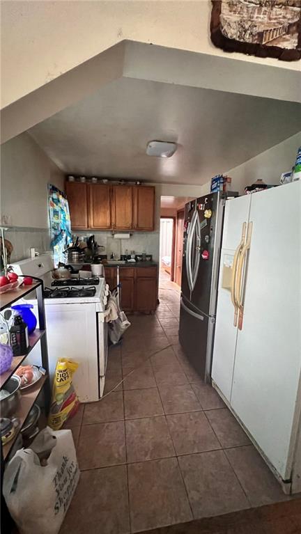 kitchen with white appliances, dark tile patterned flooring, and brown cabinets