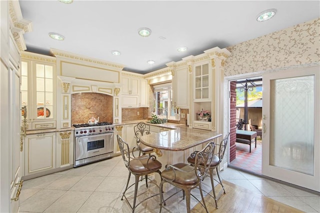 kitchen featuring a breakfast bar area, high end range, tasteful backsplash, cream cabinets, and light stone countertops