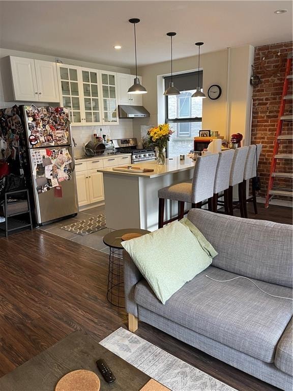 kitchen featuring tasteful backsplash, stainless steel appliances, white cabinetry, brick wall, and dark wood-type flooring