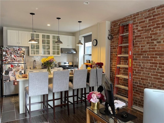 kitchen with hanging light fixtures, range, brick wall, a kitchen bar, and backsplash