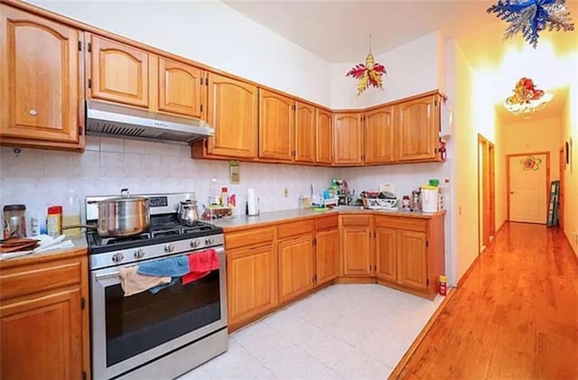 kitchen with under cabinet range hood, light countertops, decorative backsplash, brown cabinets, and gas stove