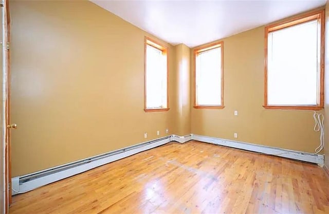 empty room with a baseboard heating unit, baseboards, and wood finished floors