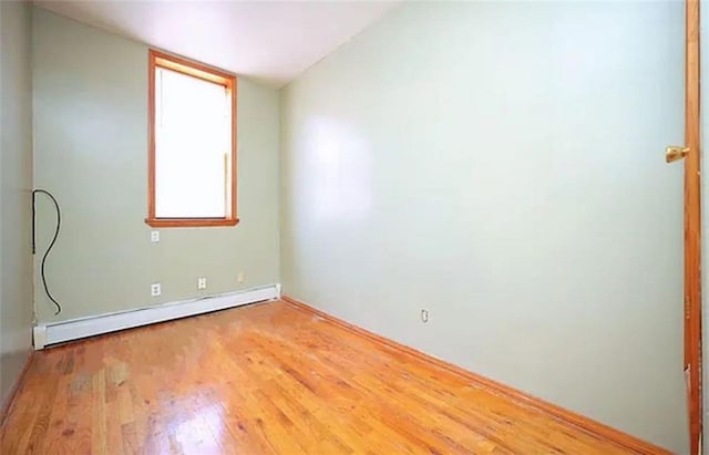 unfurnished room featuring a baseboard heating unit and wood finished floors