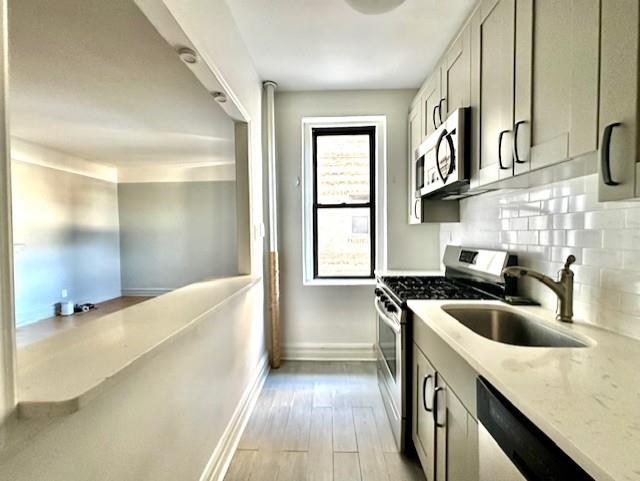 8020 4th Ave Unit D5, Brooklyn, NY 11209 - kitchen featuring appliances with stainless steel finishes, a sink, baseboards, light stone counters, and light wood-style flooring