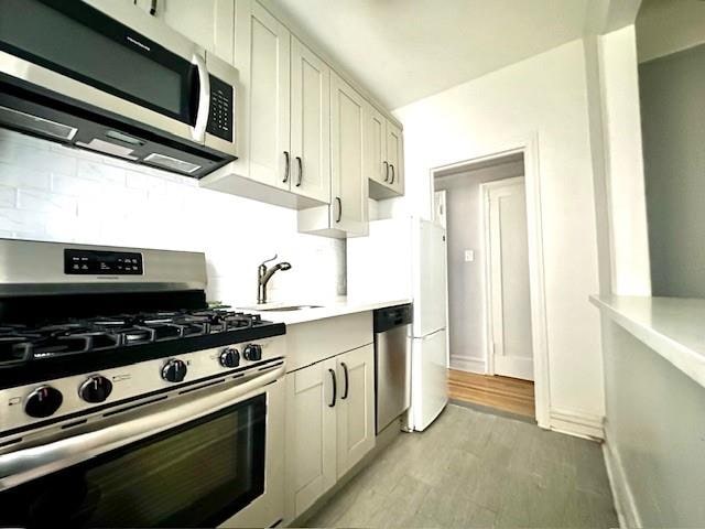 8020 4th Ave Unit D5, Brooklyn, NY 11209 - kitchen featuring appliances with stainless steel finishes, light countertops, a sink, decorative backsplash, and white cabinetry