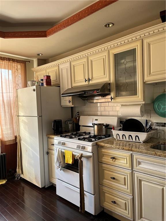 kitchen featuring under cabinet range hood, cream cabinetry, white appliances, and dark wood-type flooring