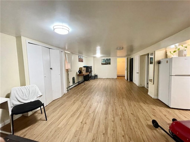 interior space featuring a baseboard heating unit, light wood finished floors, freestanding refrigerator, and baseboards