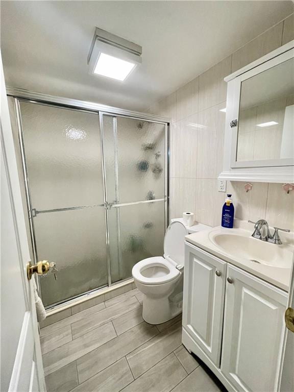 bathroom featuring toilet, a shower stall, tile walls, and vanity