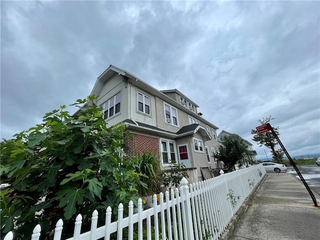 view of property exterior with a fenced front yard, brick siding, and stucco siding