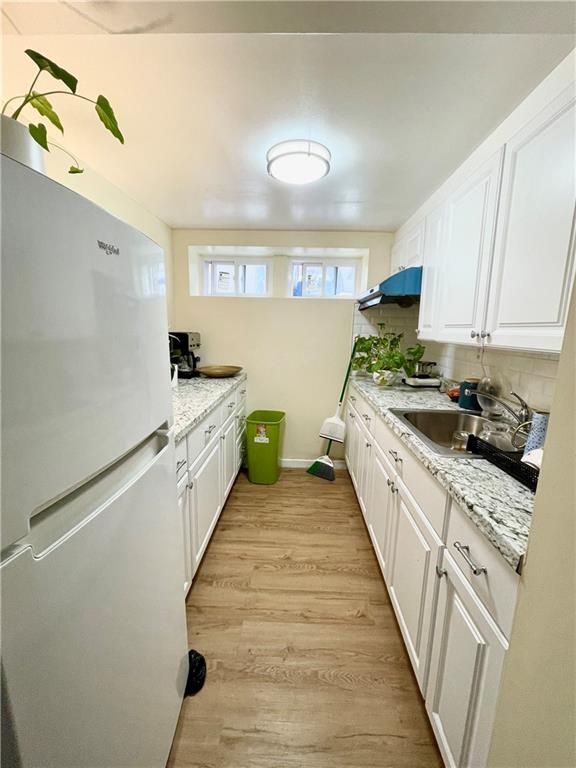 kitchen with a sink, white cabinets, backsplash, freestanding refrigerator, and light wood finished floors