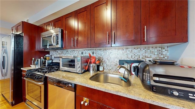 kitchen featuring light stone countertops, appliances with stainless steel finishes, light wood-type flooring, backsplash, and sink