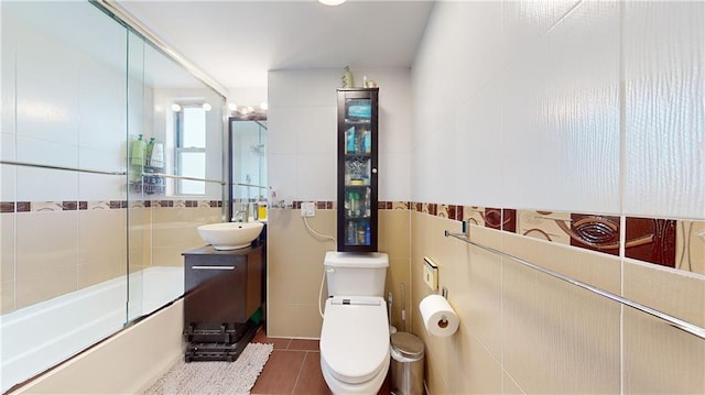 full bathroom with tile patterned floors, combined bath / shower with glass door, toilet, and tile walls