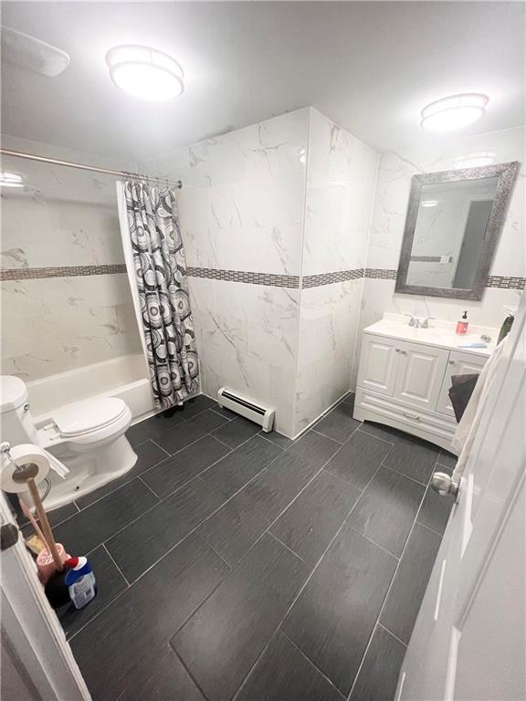 full bathroom with vanity, toilet, tile walls, baseboard heating, and shower / tub combo with curtain