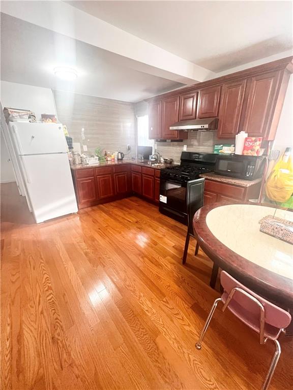 kitchen featuring backsplash, sink, black appliances, and light wood-type flooring