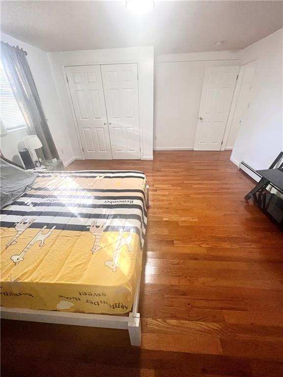 unfurnished bedroom with wood-type flooring, a baseboard radiator, and a closet