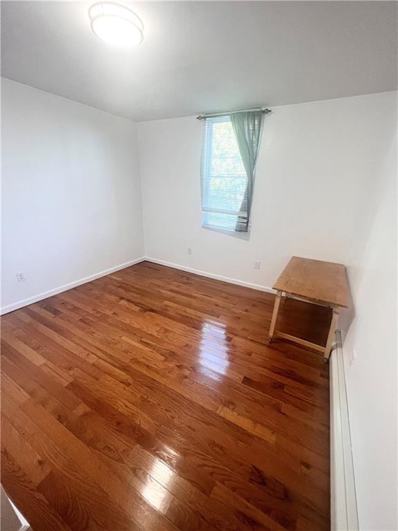 unfurnished room with dark hardwood / wood-style flooring and a baseboard heating unit