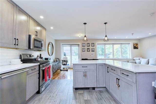 kitchen featuring a wealth of natural light, gray cabinets, hanging light fixtures, and appliances with stainless steel finishes