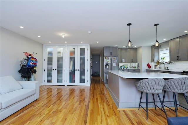 kitchen with gray cabinetry, stainless steel fridge with ice dispenser, hanging light fixtures, and a spacious island