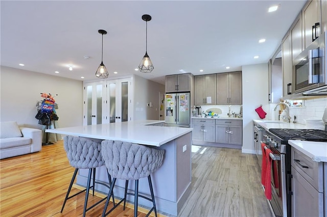 kitchen with gray cabinetry, light hardwood / wood-style floors, pendant lighting, a kitchen island, and appliances with stainless steel finishes