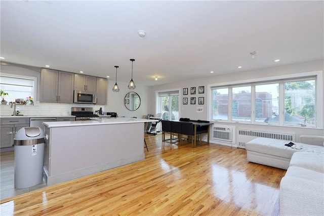 kitchen with a center island, radiator, hanging light fixtures, gray cabinets, and appliances with stainless steel finishes