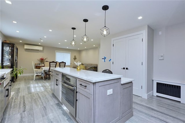 kitchen featuring gray cabinetry, hanging light fixtures, a wall unit AC, oven, and a kitchen island