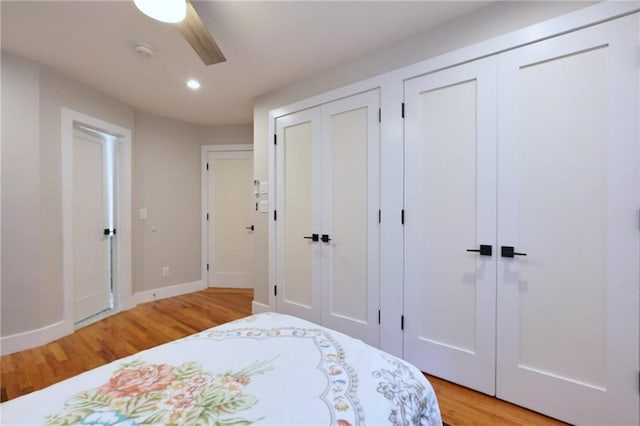 bedroom with ceiling fan, light hardwood / wood-style flooring, and two closets