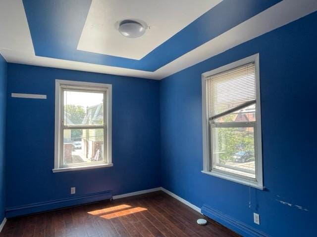 unfurnished room with baseboard heating, a tray ceiling, and dark wood-type flooring