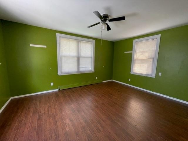 empty room with a baseboard heating unit, dark wood-type flooring, and ceiling fan