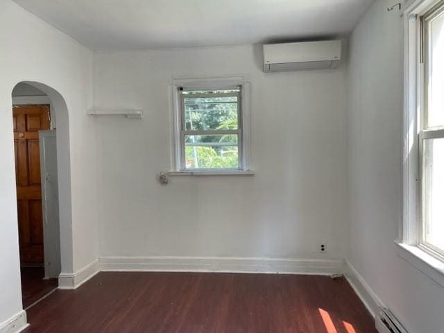 spare room with a wall mounted air conditioner, dark wood-type flooring, and a baseboard heating unit