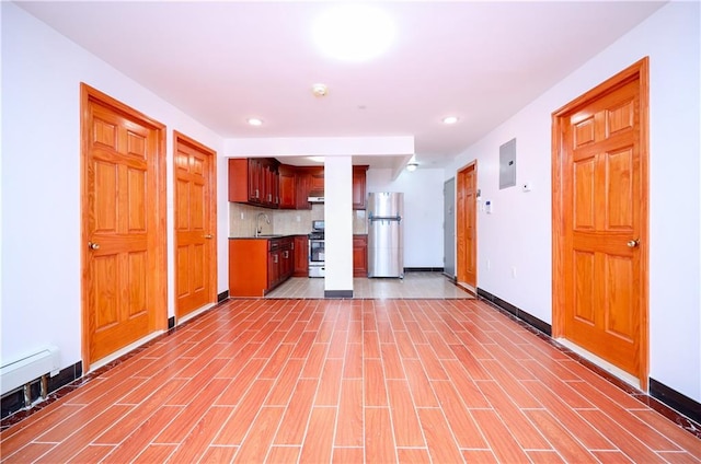 kitchen featuring stainless steel appliances, light wood-style flooring, decorative backsplash, a sink, and electric panel