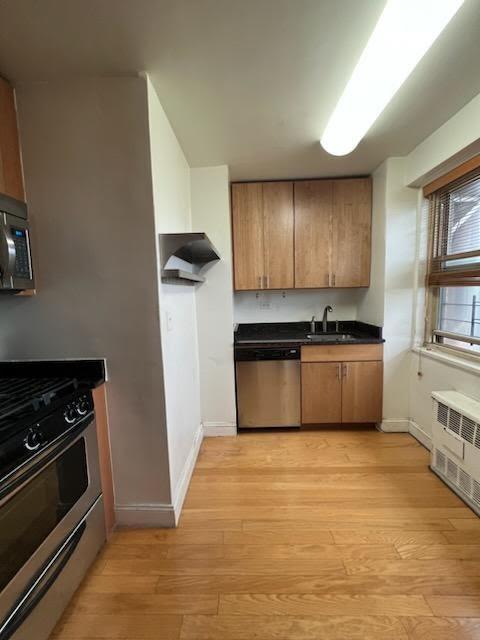 kitchen with light wood-style flooring, radiator heating unit, a sink, stainless steel appliances, and dark countertops