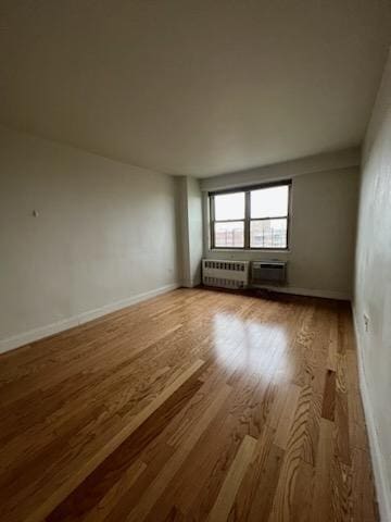 empty room with radiator, a wall mounted AC, baseboards, and wood finished floors