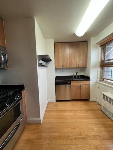 kitchen featuring dark countertops, light wood-style flooring, appliances with stainless steel finishes, and radiator heating unit