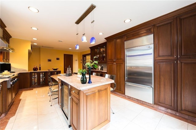 kitchen with light tile patterned floors, stainless steel appliances, hanging light fixtures, light stone countertops, and a kitchen island