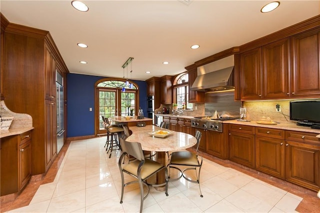 kitchen with decorative light fixtures, wall chimney range hood, stainless steel appliances, french doors, and light tile patterned floors