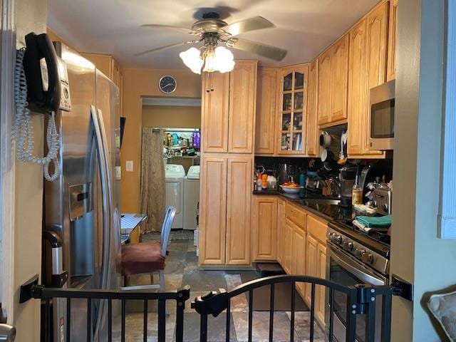 kitchen featuring dark countertops, glass insert cabinets, light brown cabinetry, washing machine and dryer, and stainless steel appliances