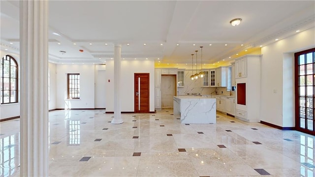 kitchen featuring ornate columns, white cabinetry, a center island, light stone countertops, and decorative light fixtures