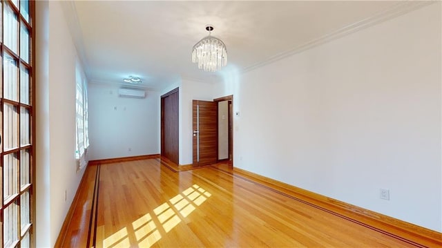 spare room featuring a chandelier, hardwood / wood-style flooring, an AC wall unit, and crown molding