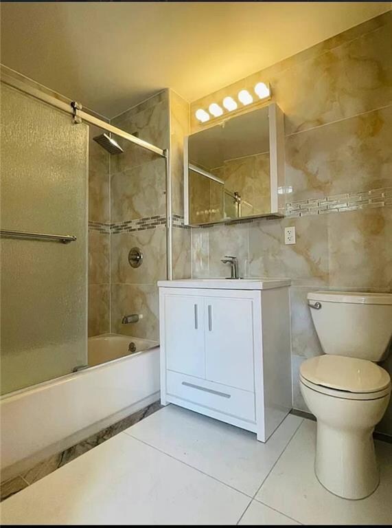 full bathroom with vanity, shower / bath combination with glass door, tile walls, tile patterned flooring, and toilet