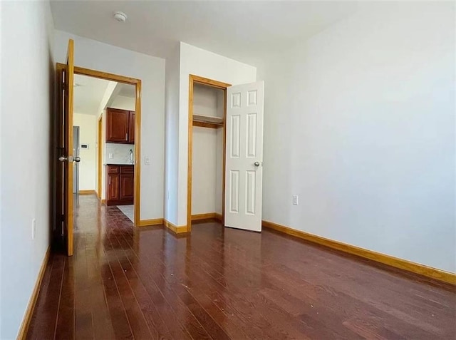 unfurnished bedroom with dark wood-type flooring, a closet, and baseboards