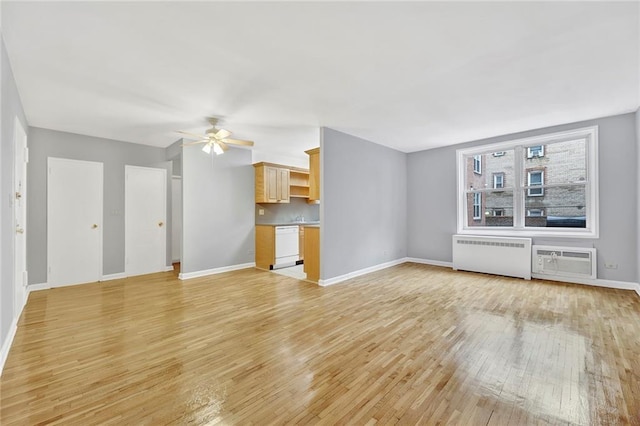 unfurnished living room with radiator, ceiling fan, baseboards, an AC wall unit, and light wood-type flooring