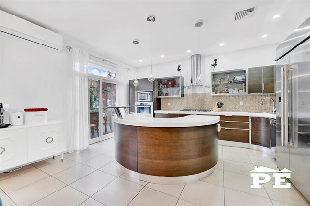 kitchen featuring stainless steel appliances, wall chimney range hood, tasteful backsplash, decorative light fixtures, and light tile patterned floors