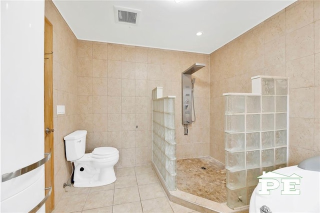 bathroom featuring tile patterned floors, toilet, a tile shower, and tile walls