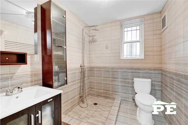 bathroom featuring toilet, a tile shower, tile walls, and vanity