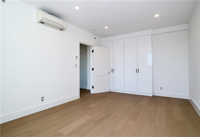 unfurnished bedroom featuring an AC wall unit, recessed lighting, light wood-style flooring, and baseboards