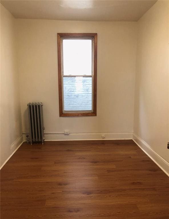 empty room featuring baseboards, radiator, and dark wood finished floors