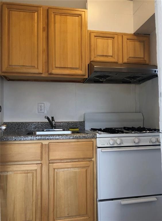 kitchen with under cabinet range hood, white range with gas cooktop, dark stone countertops, and a sink