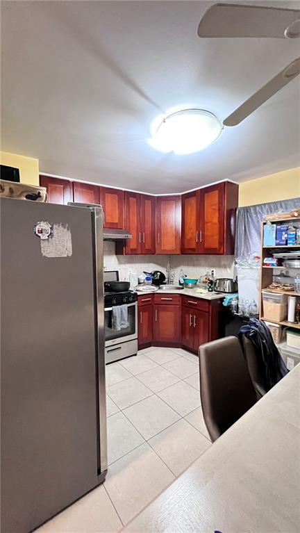 kitchen with under cabinet range hood, light countertops, light tile patterned flooring, stainless steel appliances, and reddish brown cabinets