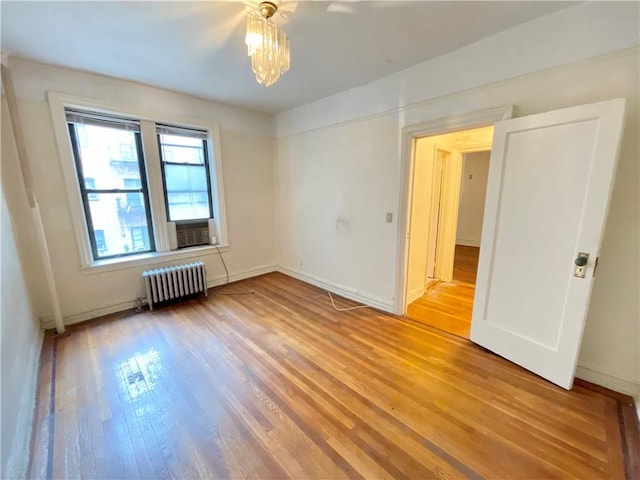 unfurnished room with radiator, hardwood / wood-style floors, and an inviting chandelier